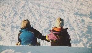 Young girl and boy sledding down a small hill
